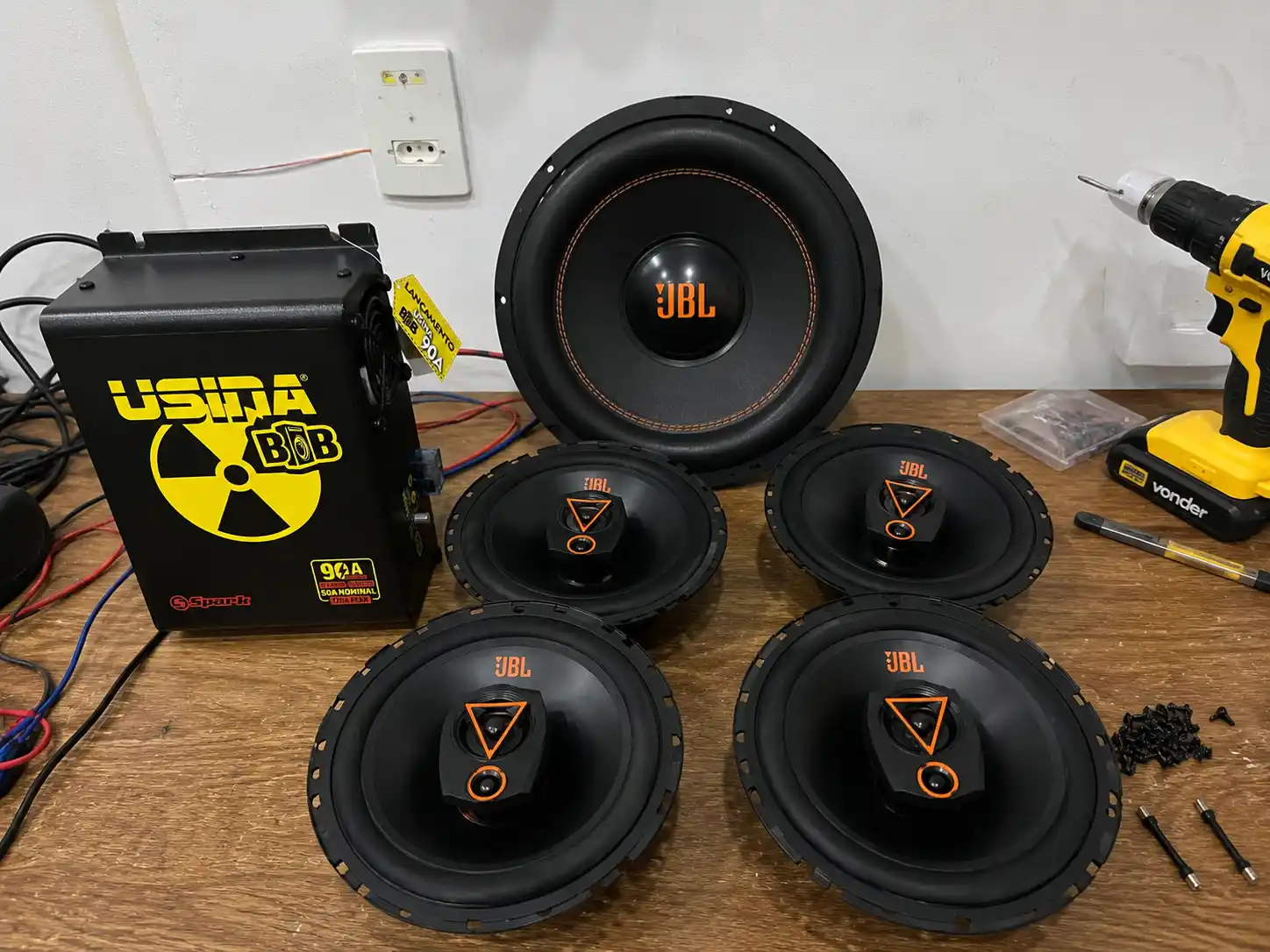 "Usina BOB 90A com alto-falantes JBL e subwoofer JBL sobre mesa de instalação de som automotivo com fios e ferramentas"